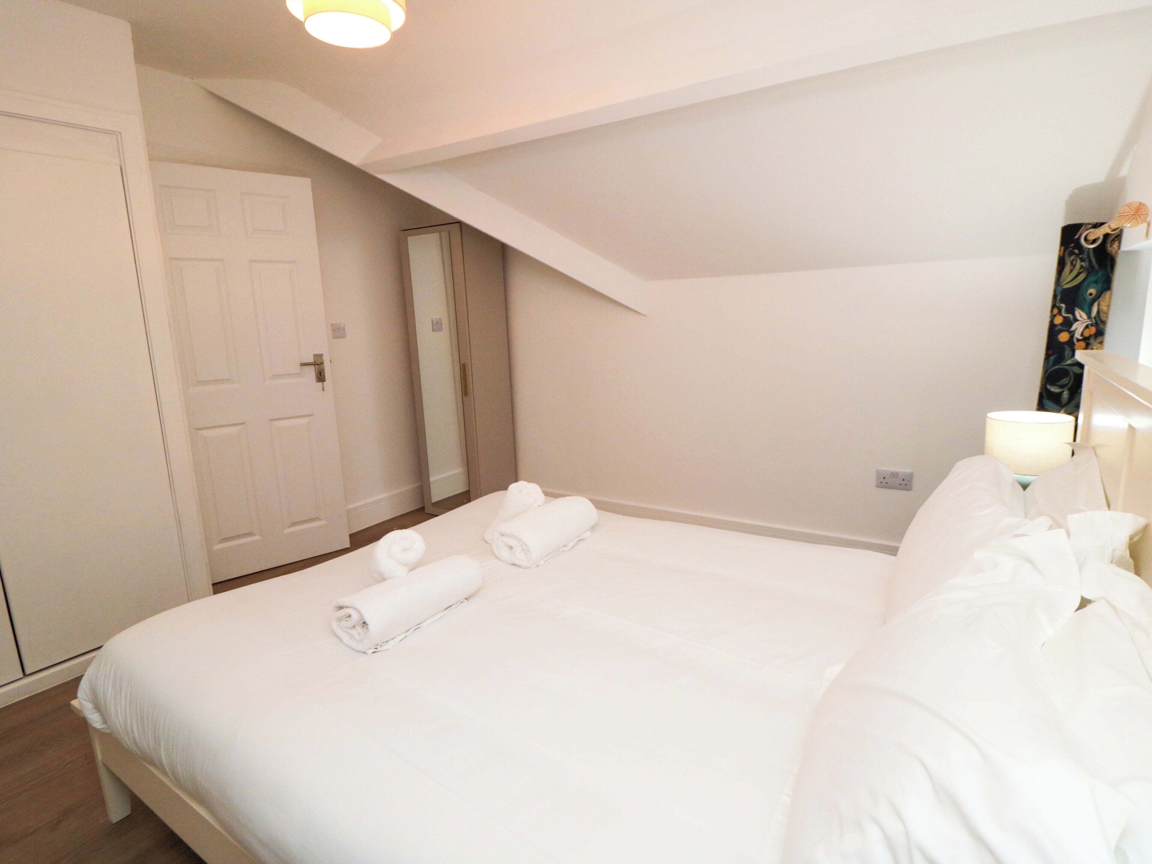 A bedroom with a large bed, a door, a mirror, and a nightstand with a lamp.