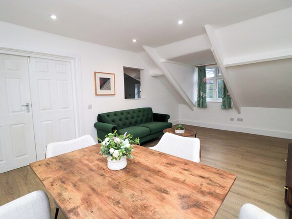 A modern living room with a green sofa, a wooden dining table with a vase of flowers, and a white door. - Beachwalk Villa 3 (Whitby)