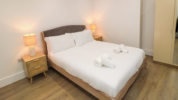 Ein ordentlich gemachtes Bett mit weißen Leinen, zwei Nachttischlampen und einem Holznachttisch.