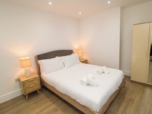A neatly made bed with white linens, two bedside lamps, and a wooden nightstand. - Beachwalk Villa 2 (Whitby)