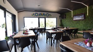 Un restaurant doté de nombreuses tables et chaises, d’un mur végétal orné de motifs floraux et d’une enseigne sur laquelle on peut lire : « Dobri mȃl Kiełdrowice ».