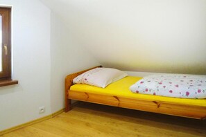 A small, single-bed room with a wooden frame, a yellow mattress, and a white pillow with a floral pattern.