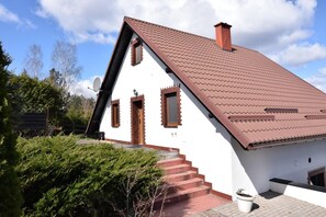 A white building with a red-tiled roof, a wooden door, and a satellite dish.