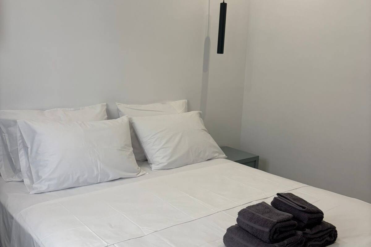 A neatly made bed with white linens, a bedside table, and a hanging light fixture.