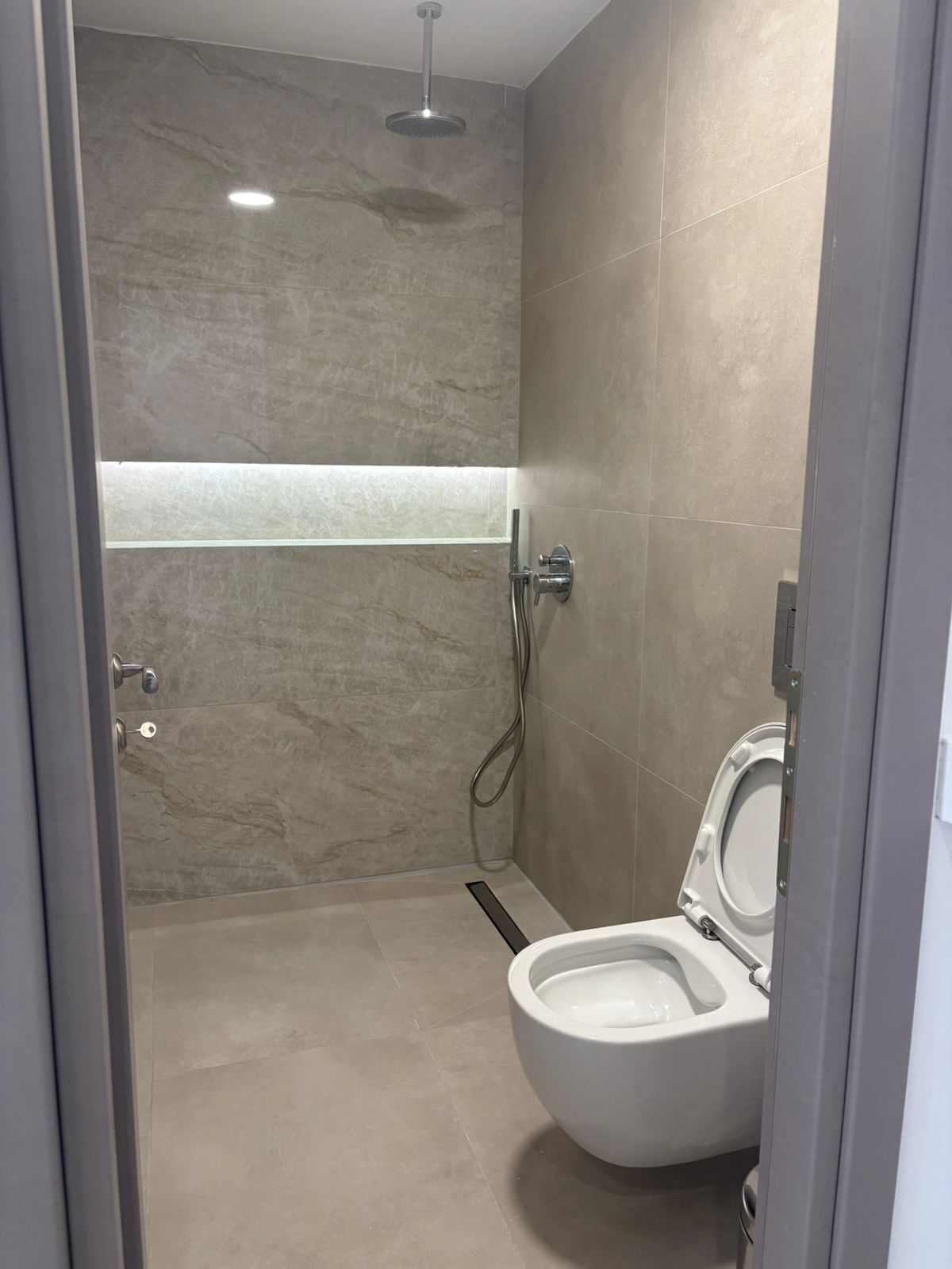 A modern bathroom with a shower, toilet, and a glass partition.