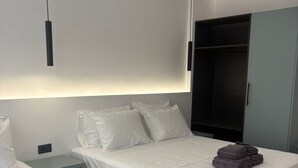 Moderni hotellihuone, jossa on kaksi sänkyä, vaatekaappi ja yöpöytä.