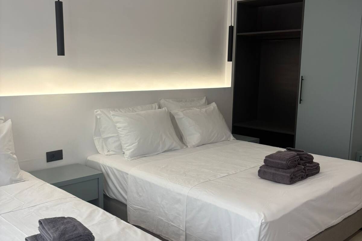 A modern hotel room with two beds, a wardrobe, and a bedside table.