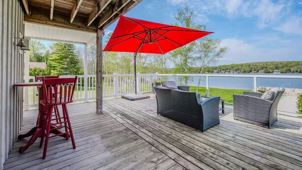 Une terrasse en bois avec des meubles d’extérieur et un parasol rouge.