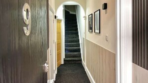 A hallway with a carpeted staircase, a wooden door, and framed pictures on the wall. - Apartment No.3 @Worcester House & Free Parking (Worcester)