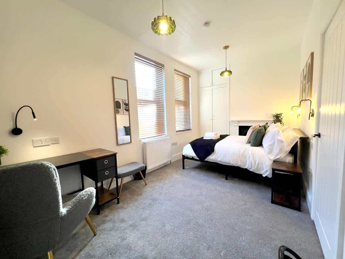 A bedroom with a bed, desk, chair, and two pendant lights.