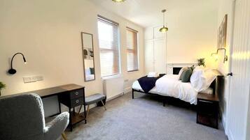 A bedroom with a bed, desk, chair, and two pendant lights.