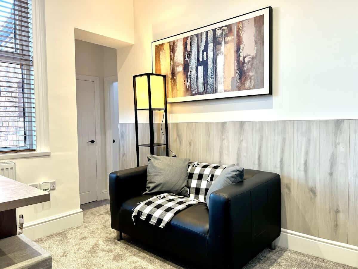 Een moderne woonkamer met een zwarte leren bank, een geruit plaid en een abstract schilderij op de muur.