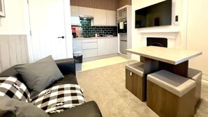 A compact living space with a kitchenette, a sofa with patterned cushions, and a small table. - Apartment No.3 @Worcester House & Free Parking (Worcester)