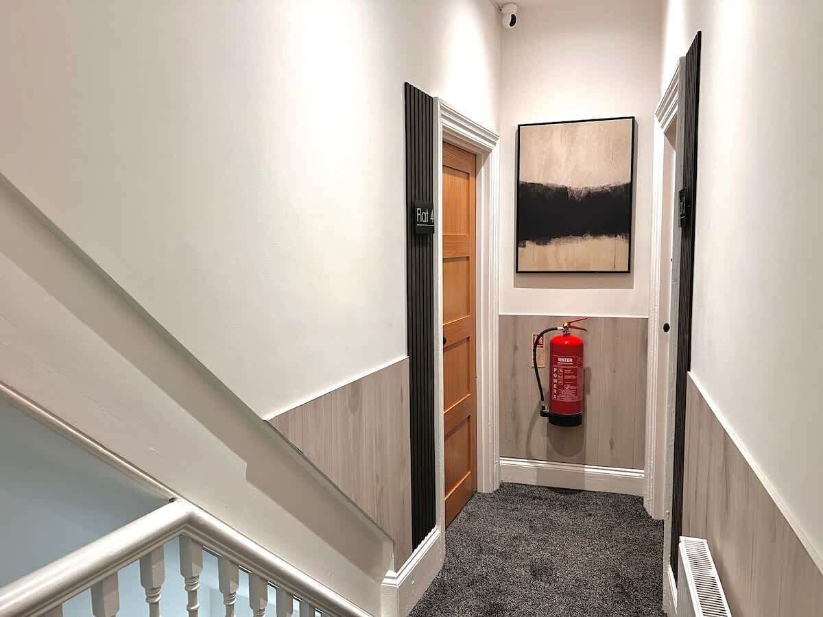 A hallway with a wooden door labeled "Flat 4," a fire extinguisher mounted on the wall, and a painting above the door.