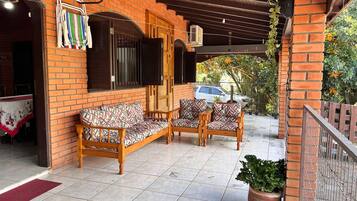 A covered patio with a brick wall, wooden furniture, and potted plants.