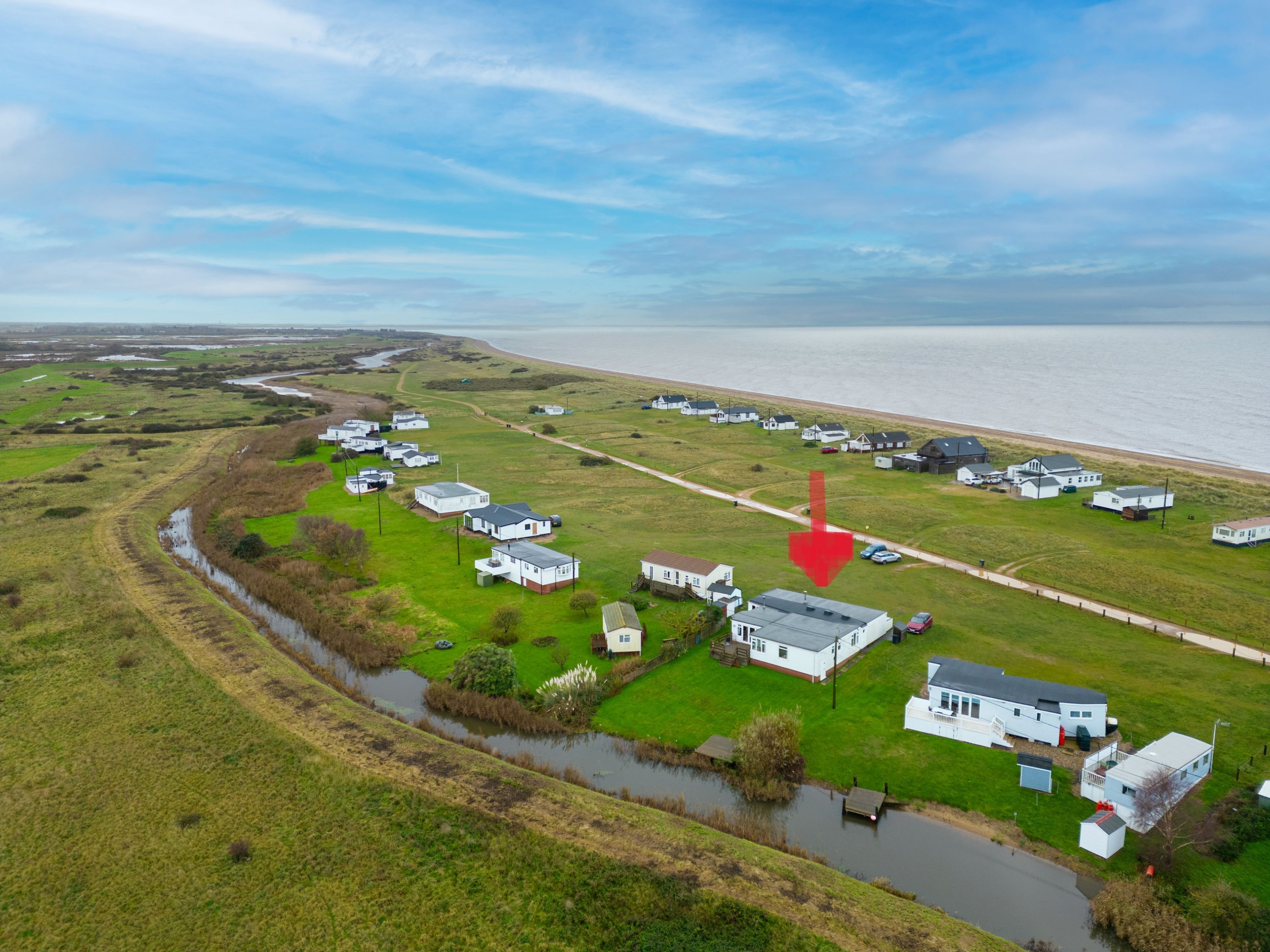 An aerial view of a coastal area with white mobile homes, a river, and a beach.