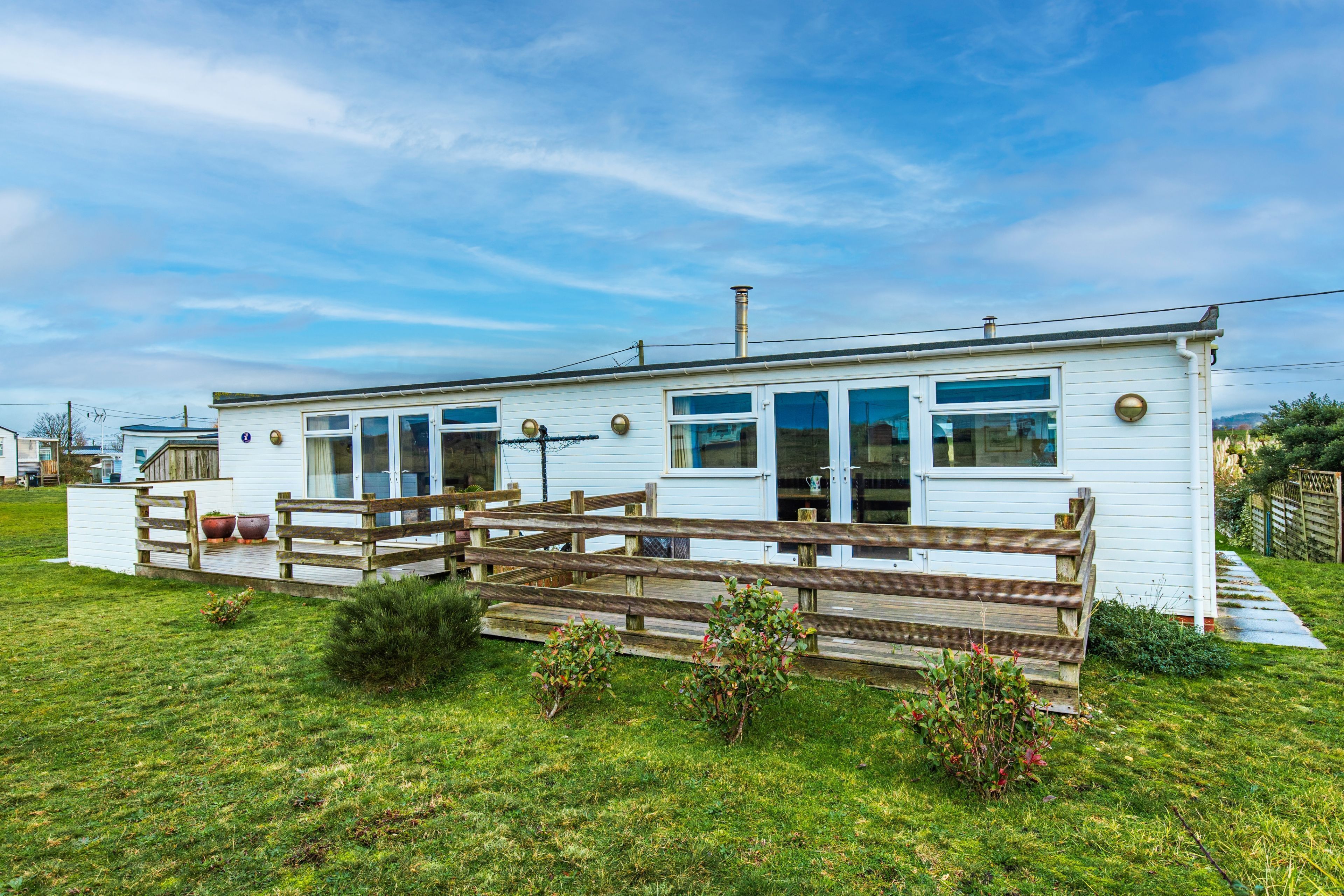 A white mobile home with a wooden deck and a fenced yard.