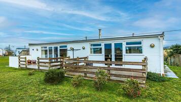 A white mobile home with a wooden deck and a fenced yard.