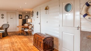A room with a wooden floor, a dining table with chairs, a small wooden chest, and a life preserver on the wall.