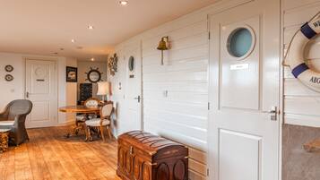 A room with a wooden floor, a dining table with chairs, a small wooden chest, and a life preserver on the wall.