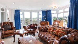 A spacious living room with leather sofas, a wooden coffee table, and a large window with blue curtains.