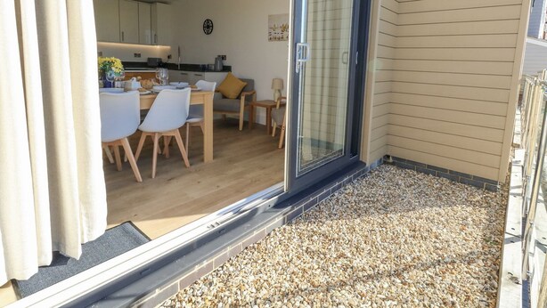 A modern interior with a dining area, kitchen, and a balcony with gravel flooring. - Sea Fern House - 36 (Poole)