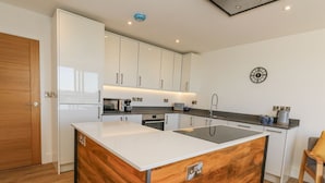 A modern kitchen with white cabinets, a central island, and a wooden accent wall. - Sea Fern House - 36 (Poole)