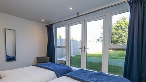 A bedroom with two beds, a chair, a large window, and a door leading to a backyard. - Sea Fern House - 36 (Poole)