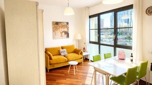 Una sala de estar moderna con un sofá amarillo, una mesa de comedor con sillas verdes y un ventanal con vistas a la ciudad.