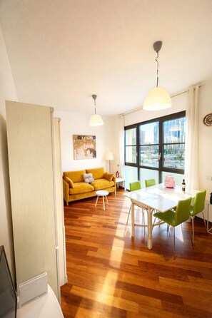 Ein modernes Wohnzimmer mit einem gelben Sofa, einem Esstisch mit grünen Stühlen und einem großen Fenster mit Blick auf die Stadt.