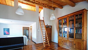 A spacious room with wooden flooring, a loft bed, a wooden bookcase, and a ladder leading to a loft area. - Open space a due passi da Oristano e dal Sinis (Milis)