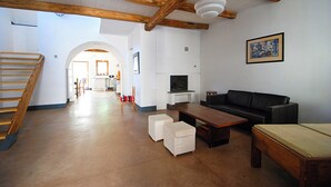 A spacious living area with a wooden staircase, a black sofa, a wooden coffee table, and a television. - Open space a due passi da Oristano e dal Sinis (Milis)