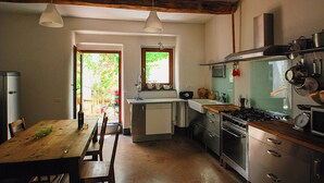 A kitchen with a wooden table, chairs, a refrigerator, a stove, and a sink. - Open space a due passi da Oristano e dal Sinis (Milis)