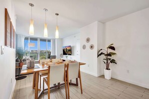 A modern dining area with a wooden table and chairs, pendant lights, and a large window with a city view. - Ocean and Canal View Condo Resort Hallandale 706 (Hallandale Beach)