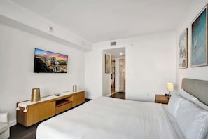 A hotel room with a large bed, a wooden console table, a flat-screen TV mounted on the wall, and a painting above the bed. - Ocean and Canal View Condo Resort Hallandale 706 (Hallandale Beach)