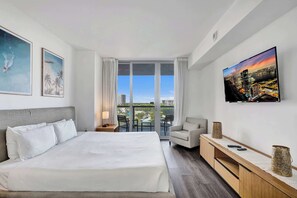 A hotel room with a large bed, a TV mounted on the wall, a balcony with a view of the city, and a desk with a lamp and decorative items. - Ocean and Canal View Condo Resort Hallandale 706 (Hallandale Beach)