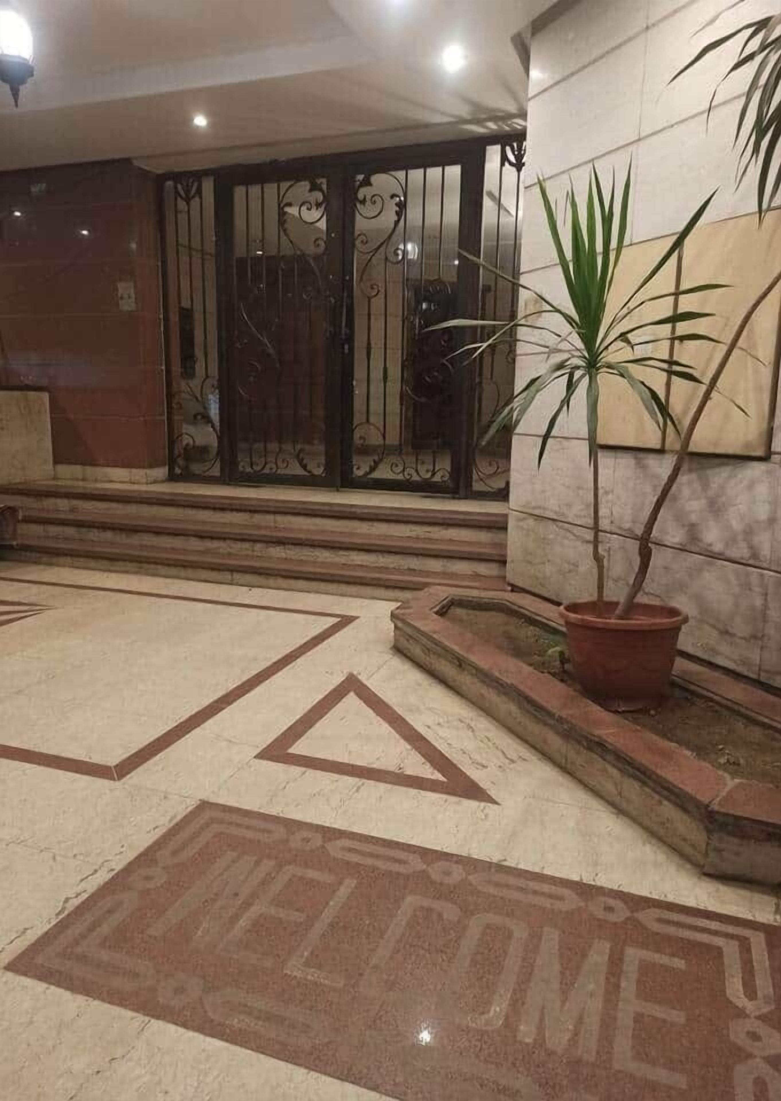 Un sol carrelé avec l’inscription « BIENVENUE », une plante en pot et un portail en métal orné de motifs décoratifs.