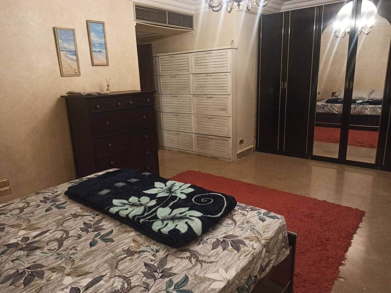 Une chambre à coucher avec un lit, une commode, une armoire et un tapis rouge.