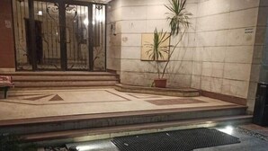 Entrada de hotel com chão de azulejos, planta em vaso e portão de metal.