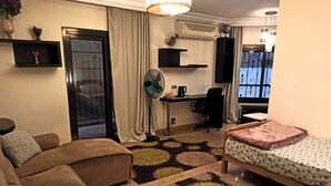 Quarto de hotel compacto com sofá, cama, escrivaninha e ventoinha.