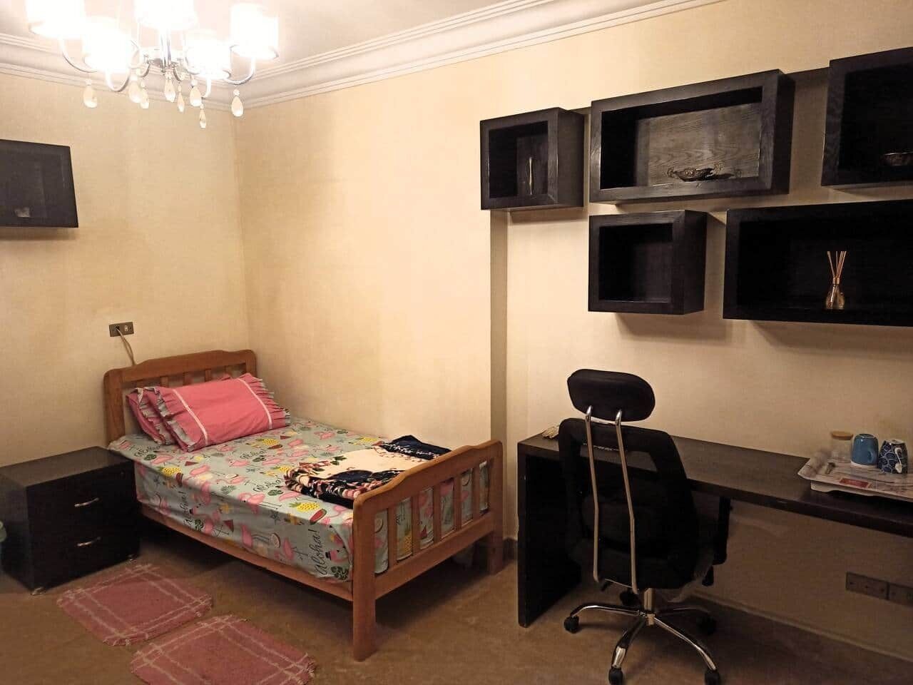 A bedroom with a bed, a desk, a chair, and shelves.