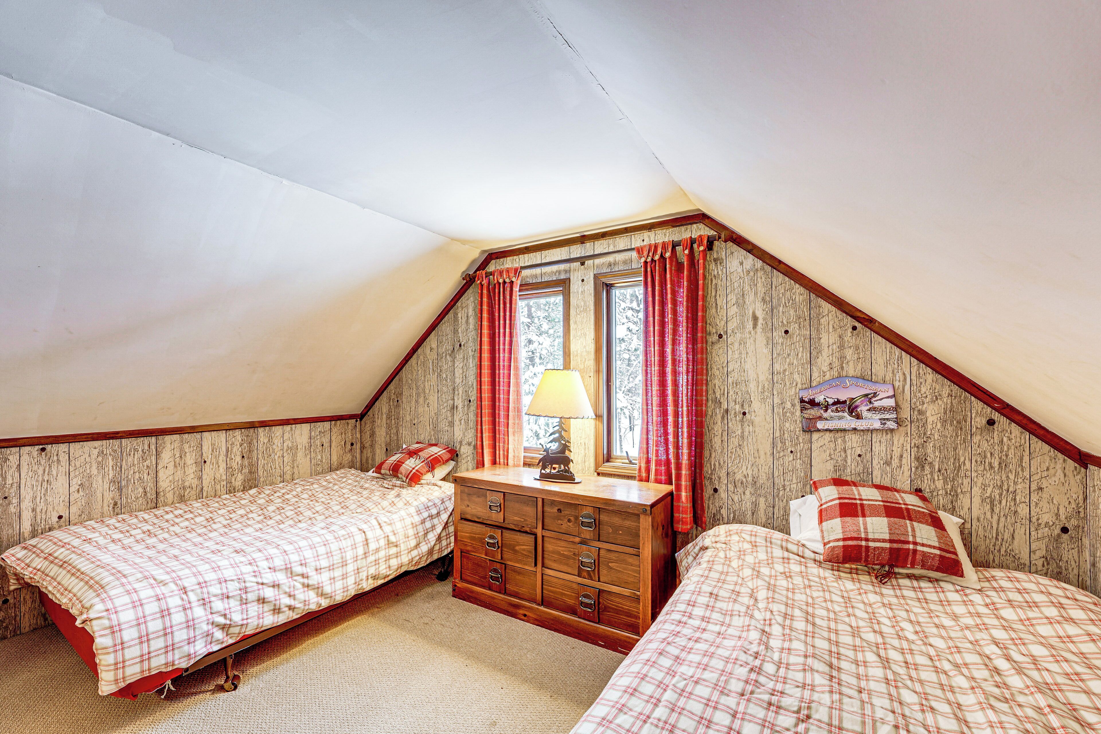 A bedroom with two beds, a dresser, and a window with curtains.