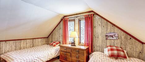 A bedroom with two beds, a dresser, and a window with curtains.