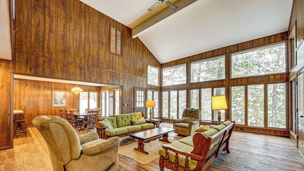 A spacious living room with wooden paneling, large windows, and comfortable seating. - Near Manistee National Forest! Retro Cabin Retreat (Baldwin)