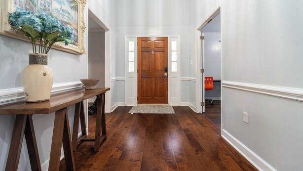 A hallway with a wooden door, a vase with flowers, and a painting on the wall. - Ballantyne Single-Story Ranch off the Greenway (Charlotte)