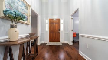Un couloir avec une porte en bois, un vase rempli de fleurs et un tableau accroché au mur.