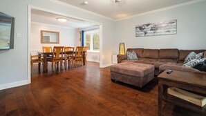 A living room with a brown leather couch, a wooden coffee table, and a dining area with a wooden table and chairs. - Ballantyne Single-Story Ranch off the Greenway (Charlotte)