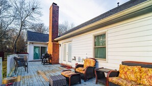 A wooden deck with outdoor furniture, a brick chimney, and a white house with a green door. - Ballantyne Single-Story Ranch off the Greenway (Charlotte)