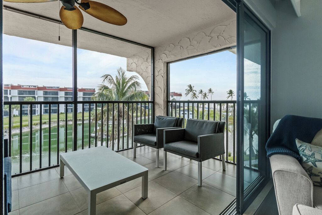 A balcony with a table and chairs, a sofa, and a view of a building and palm trees.