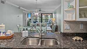 A kitchen with granite countertops, a double sink, and a dining area with light green chairs and a table. - 2 bedroom 2 bath gulf view condo at Pointe Santo (Sanibel)